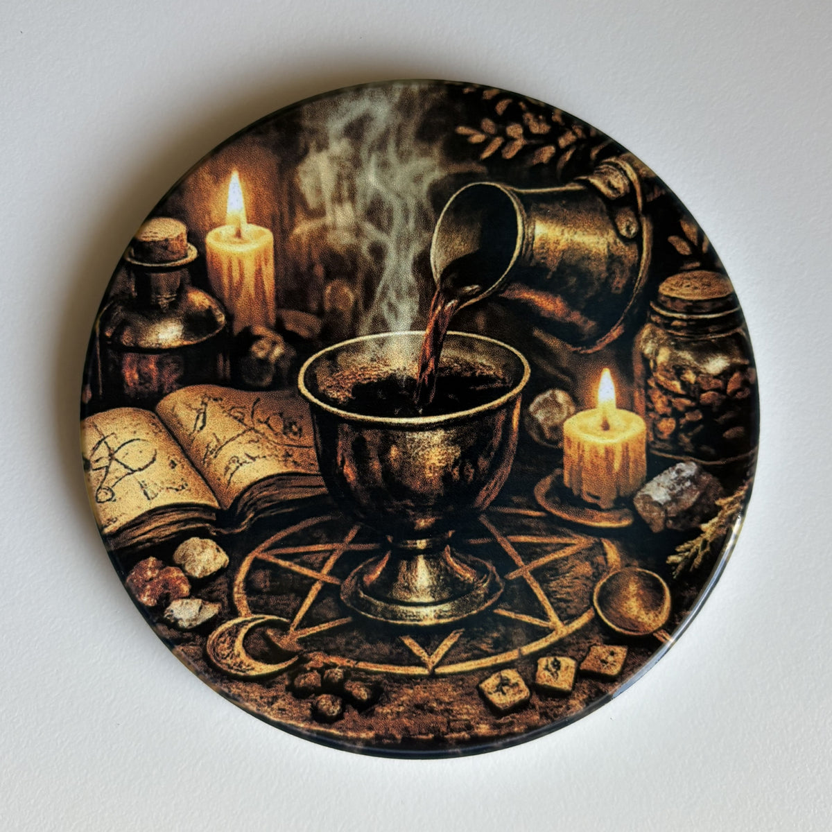 A coaster featuring a mystical illustration of a chalice with liquid being poured, surrounded by candles, an open book, jars, dice, and a pentagram on a dark background.