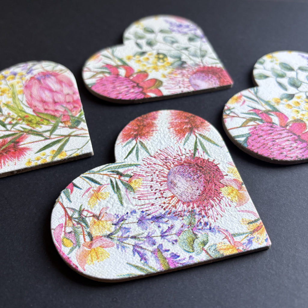 A set of heart-shaped magnets with a colorful watercolor floral print, arranged on a dark textured surface.