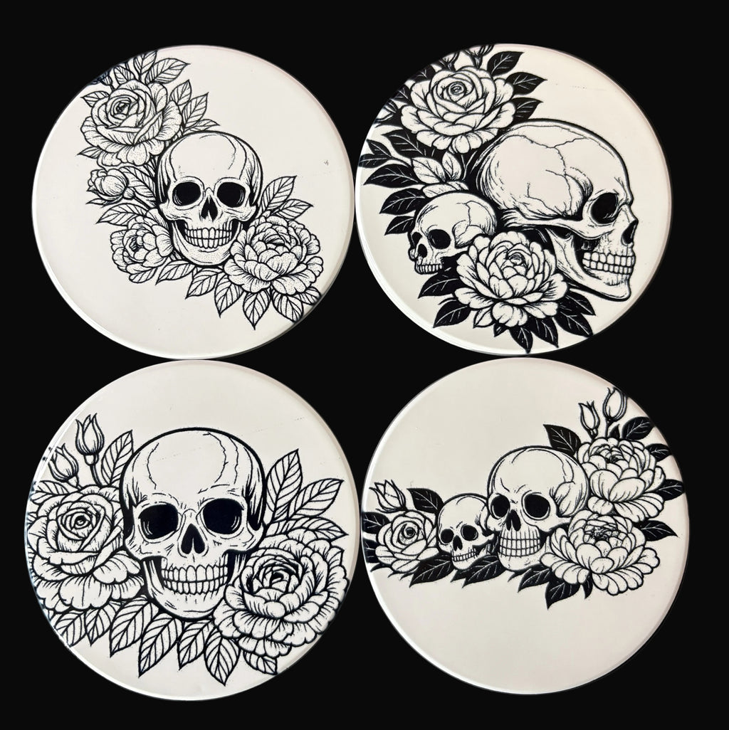 Four coasters with black and white skull and floral designs on a dark background