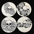Four coasters with black and white skull and floral designs on a dark background