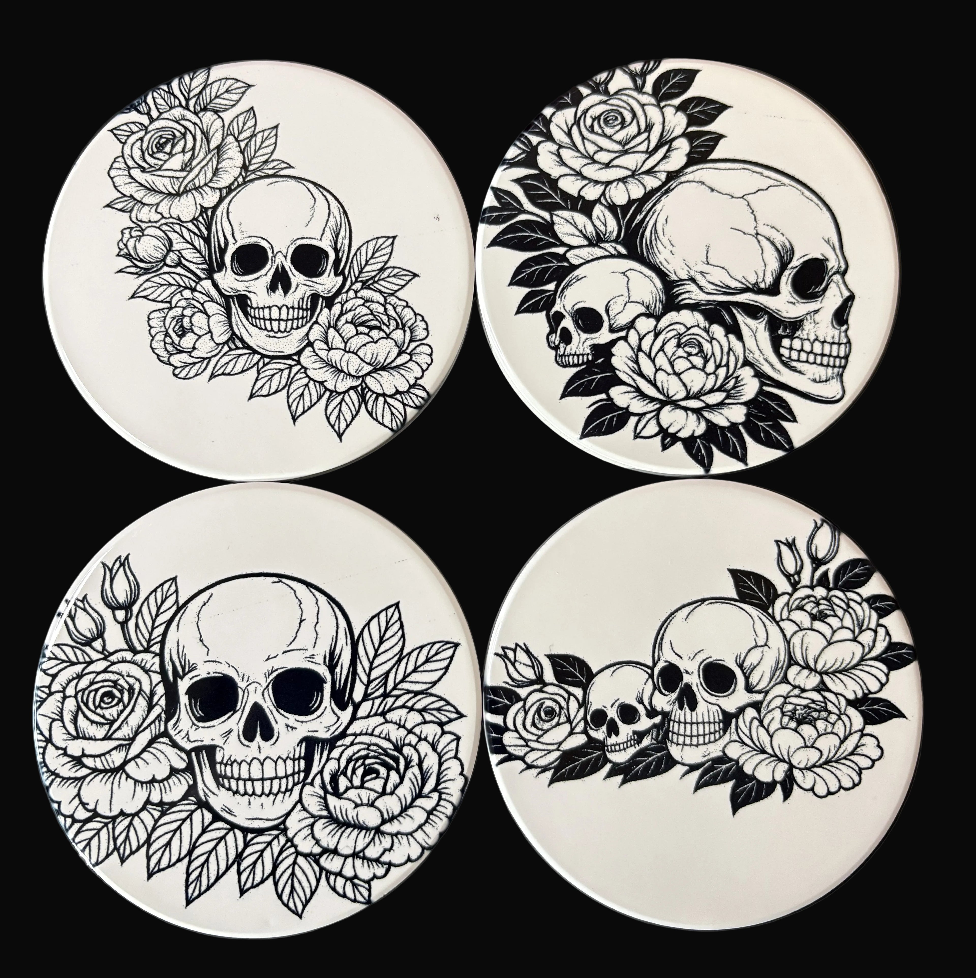 Four coasters with black and white skull and floral designs on a dark background