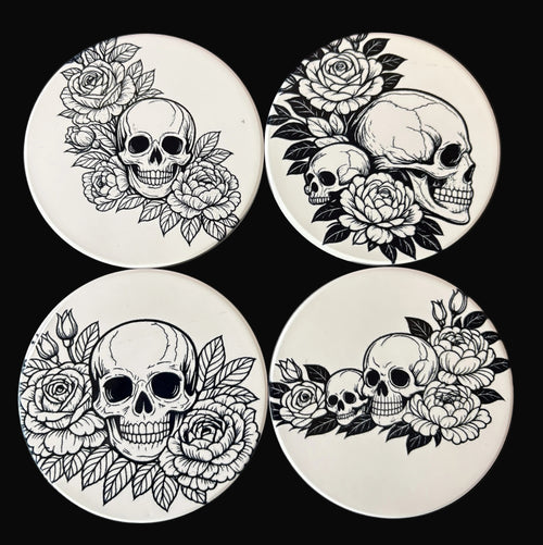 Four coasters with black and white skull and floral designs on a dark background