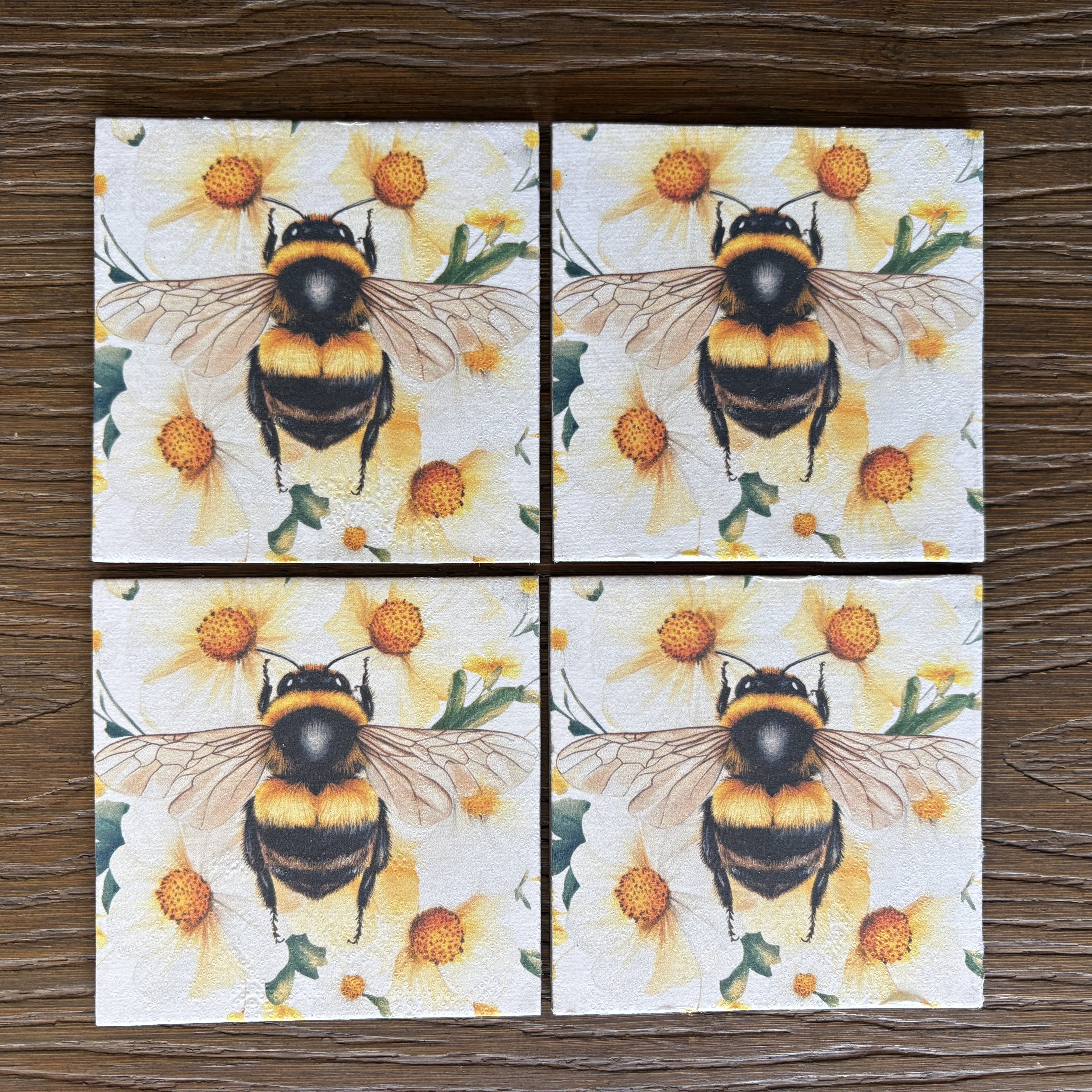 Four square magnets arranged in a 2x2 grid, each printed with a bumblebee over yellow flowers, shown on a dark wood surface.