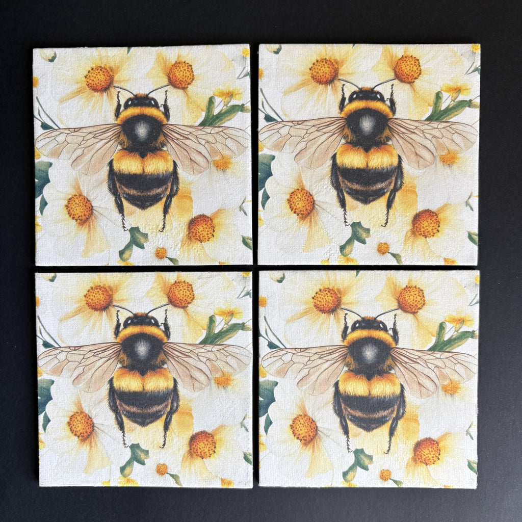Four square magnets arranged in a 2x2 grid, each printed with a large bumblebee over yellow flowers on a white background, photographed on a dark surface.