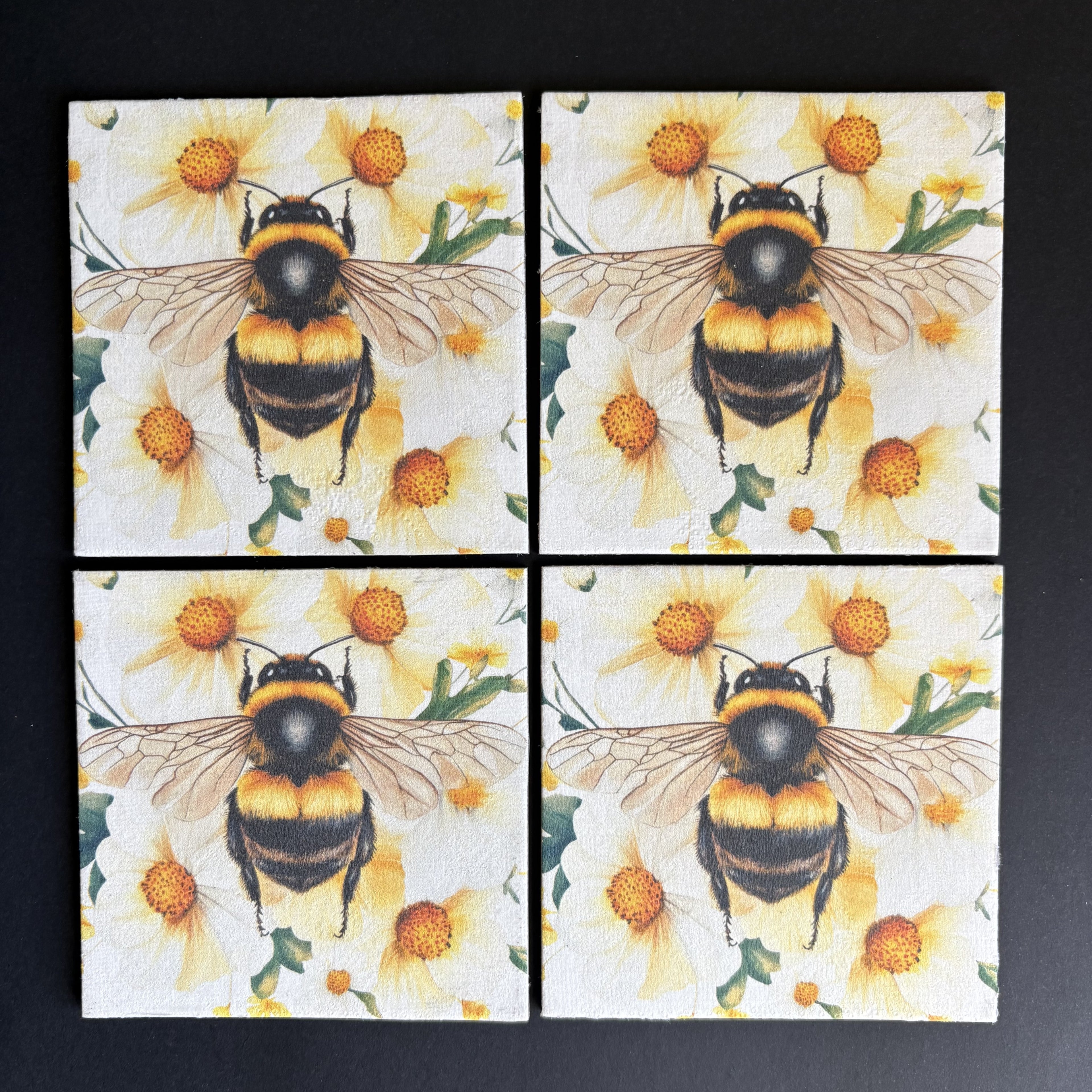 Four square magnets arranged in a 2x2 grid, each printed with a large bumblebee over yellow flowers on a white background, photographed on a dark surface.
