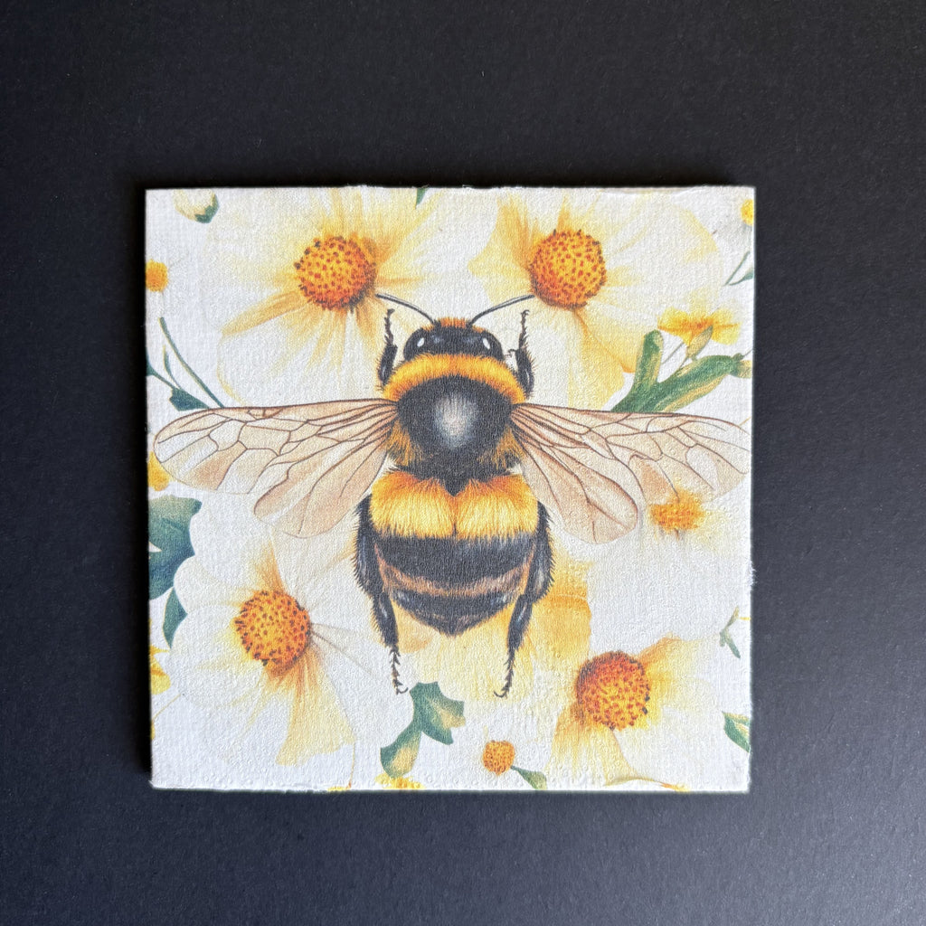 A square magnet featuring a detailed illustration of a bumblebee on a background of yellow daisies, displayed against a dark textured background.
