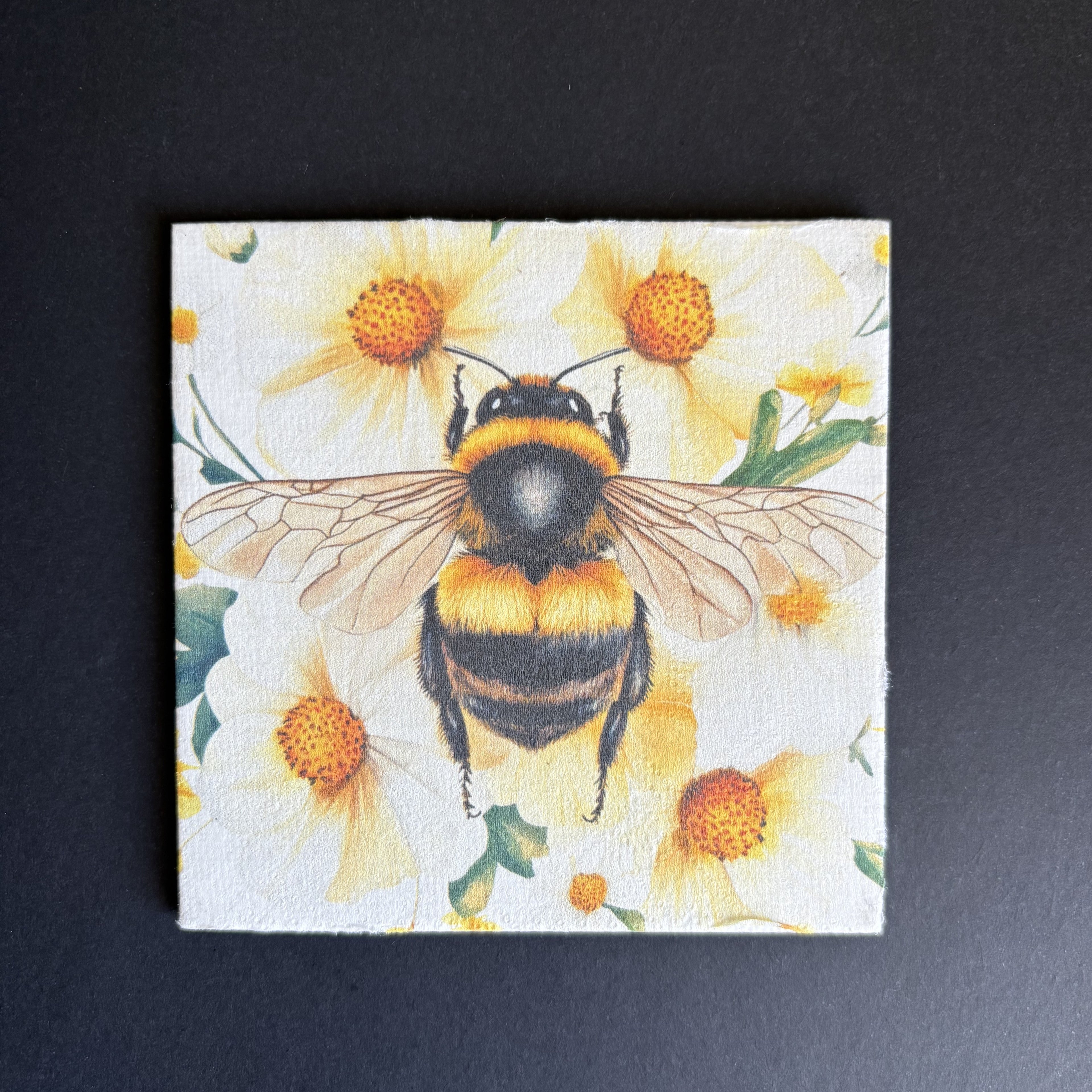 A square magnet featuring a detailed illustration of a bumblebee on a background of yellow daisies, displayed against a dark textured background.