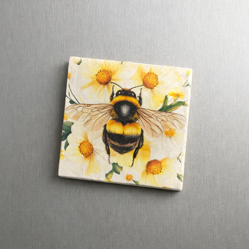 A square decorative magnet featuring a painted bumblebee over yellow flowers, photographed on a brushed silver metal surface.