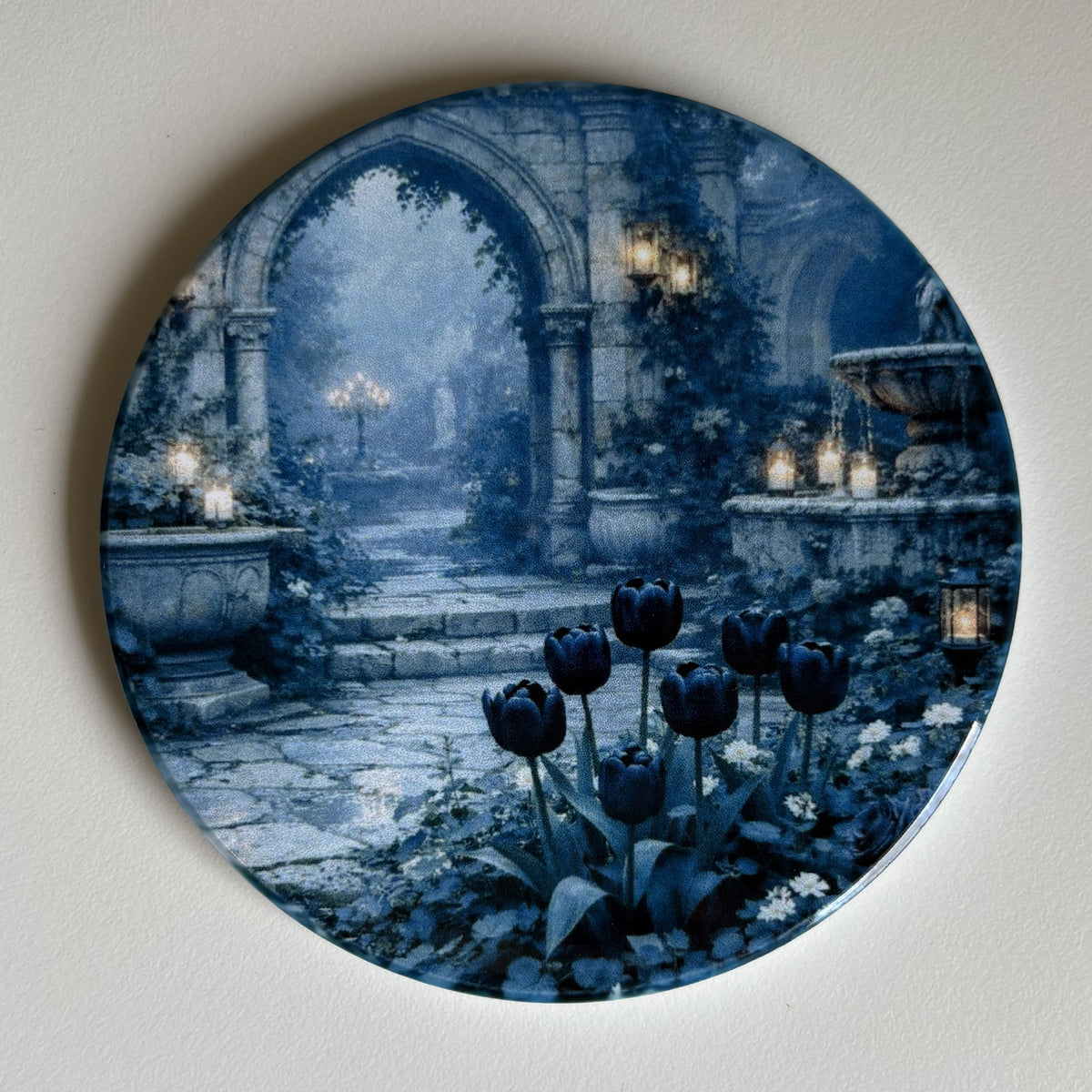 Round decorative coaster featuring a blue-toned garden scene with stone arches, lanterns, and dark blue tulips, mounted on a light beige wall.