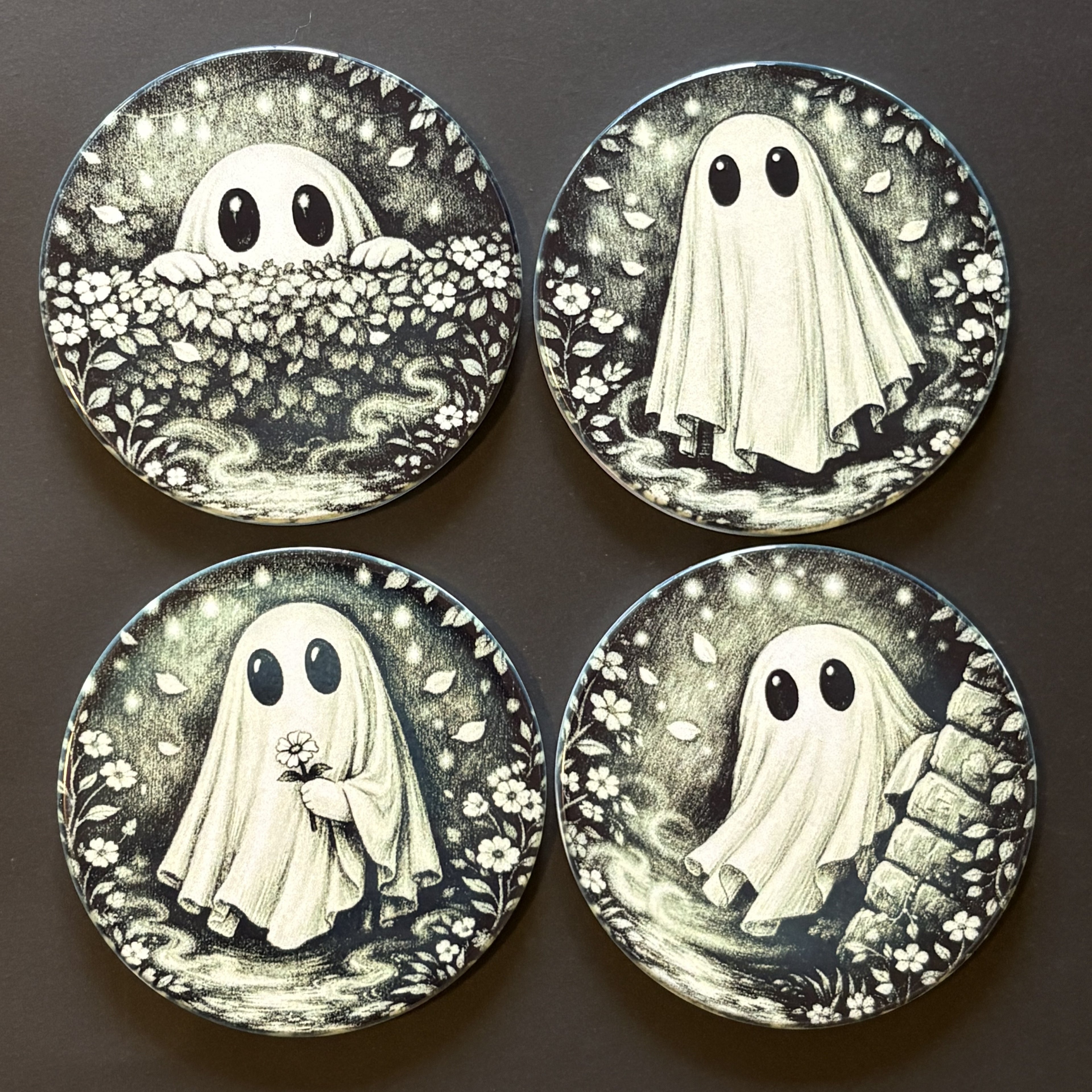 Four round decorative coasters featuring a black and white illustration of a ghost in different poses, arranged in a 2x2 grid on a dark background.