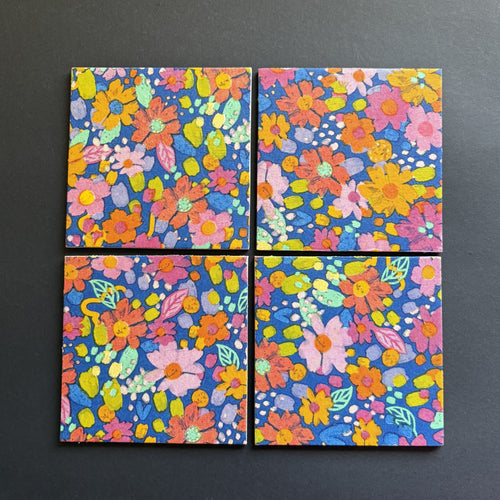 Four square magnets arranged in a 2x2 grid, featuring a vibrant, multicolored floral pattern on a dark blue background, set against a dark gray surface.