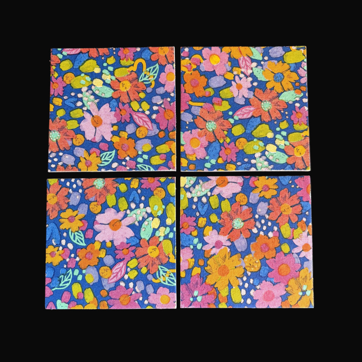 Four square floral magnets arranged in a 2x2 grid on a dark gray background. Each coaster features a vibrant multicolor floral pattern with pink, orange, yellow, and green flowers on a deep blue base.