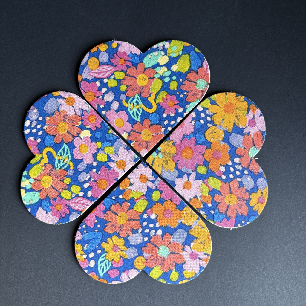 Four interlocking flower-shaped magnets with a vibrant multicolor floral pattern on a dark background, arranged in a cross shape on a dark gray surface.