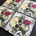 Four square magnet arranged in a grid, each printed with a skull over crossed bones, black eye sockets, and a red rose with green leaves on a dark background.
