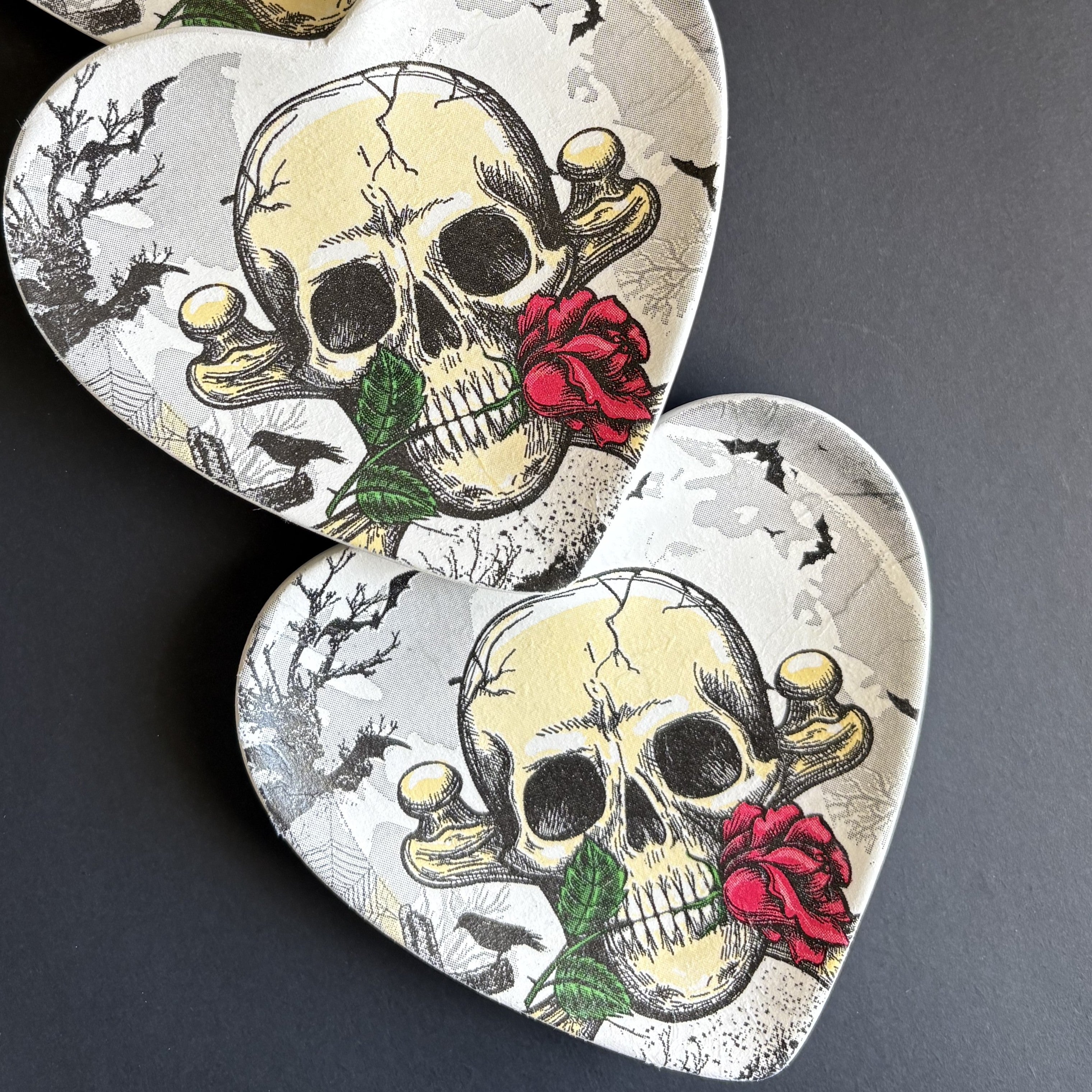 Two heart-shaped trinket tray featuring a vintage-style skull illustration with a red rose, displayed on a dark gray background.