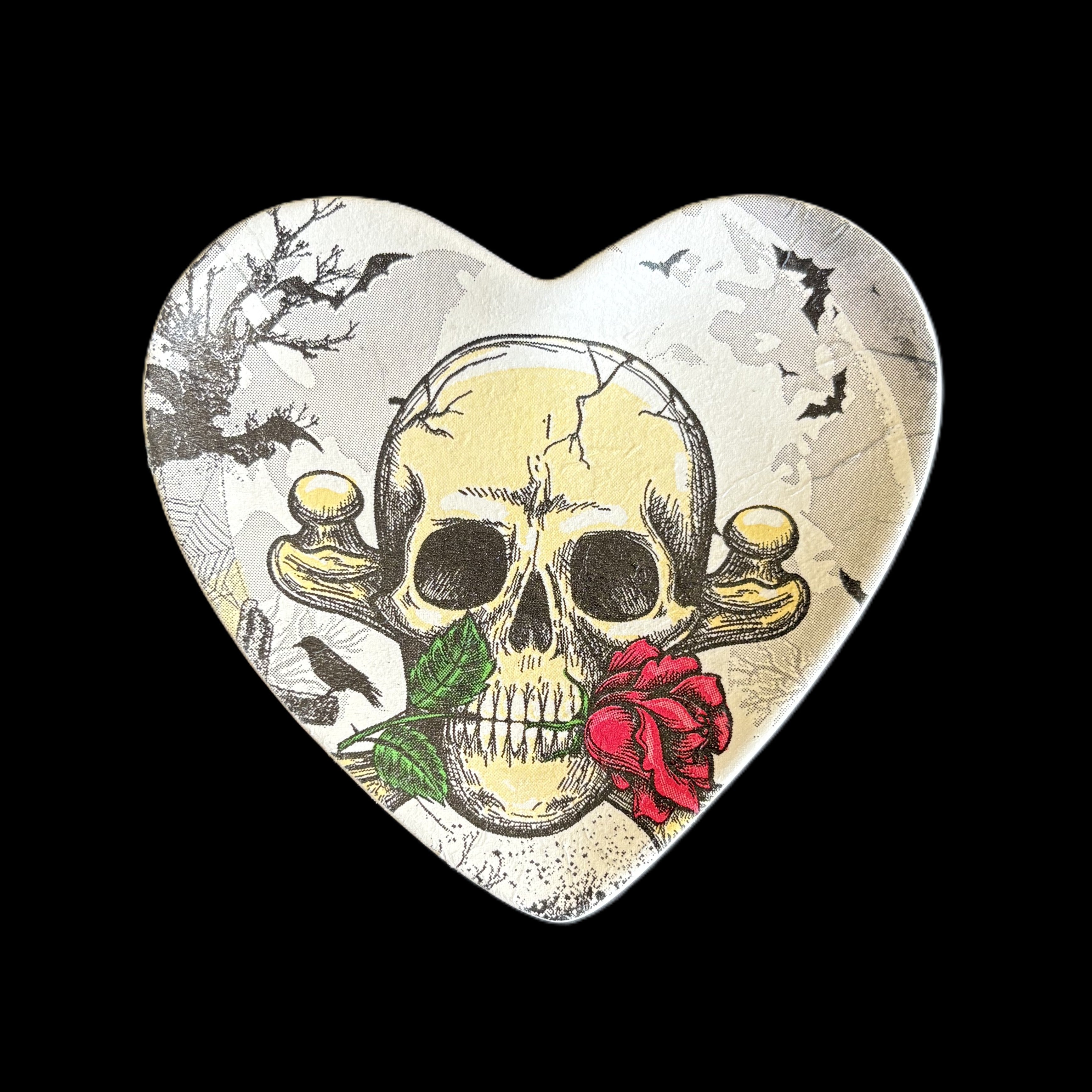 A heart-shaped decorative trinket tray featuring a vintage-style illustration of a skull with a red rose and green leaves, set against a black background.