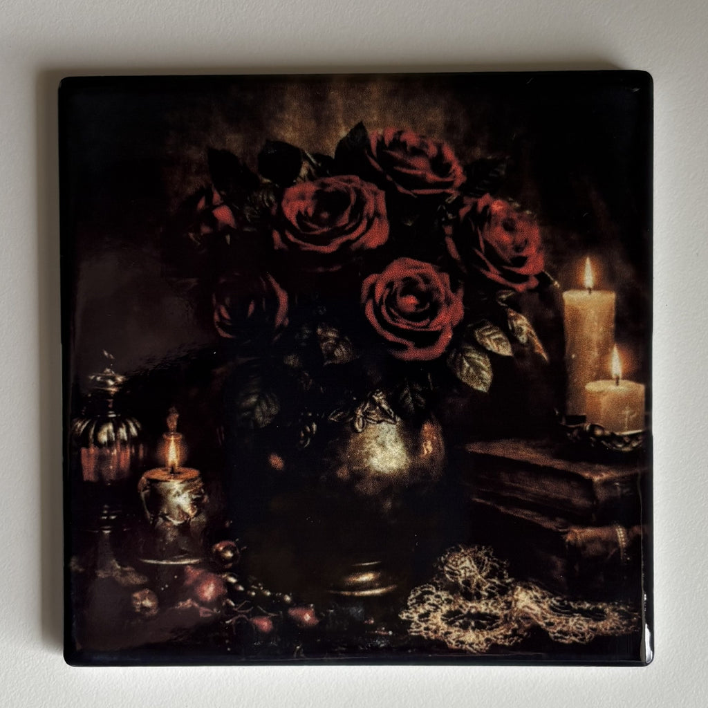 A square coaster featuring a dark gothic still life painting of red roses in a vase, surrounded by lit candles, books, and a gold chain, shown on a light gray background.