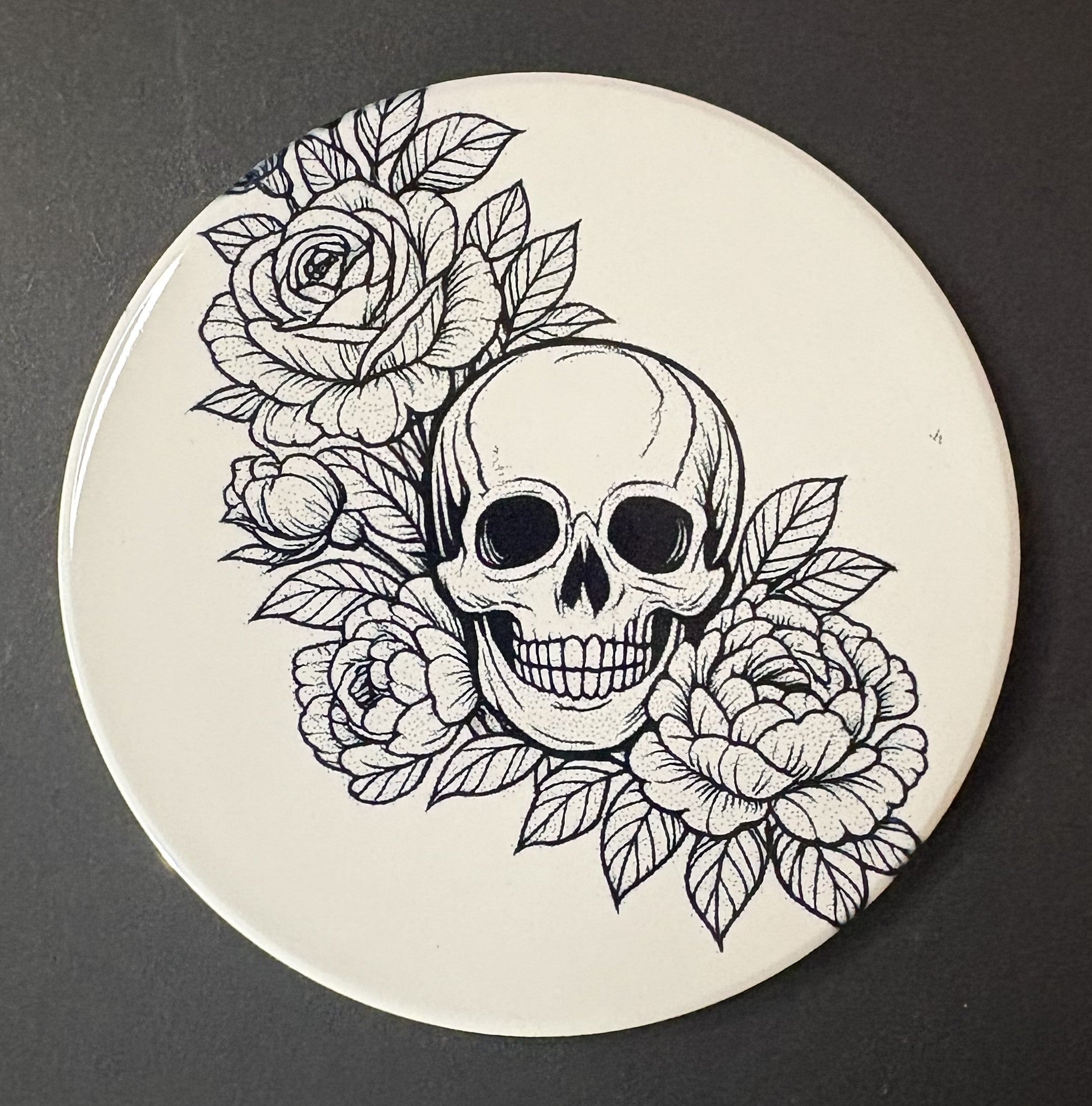 Circular coaster with a black and white skull and floral design on a dark background