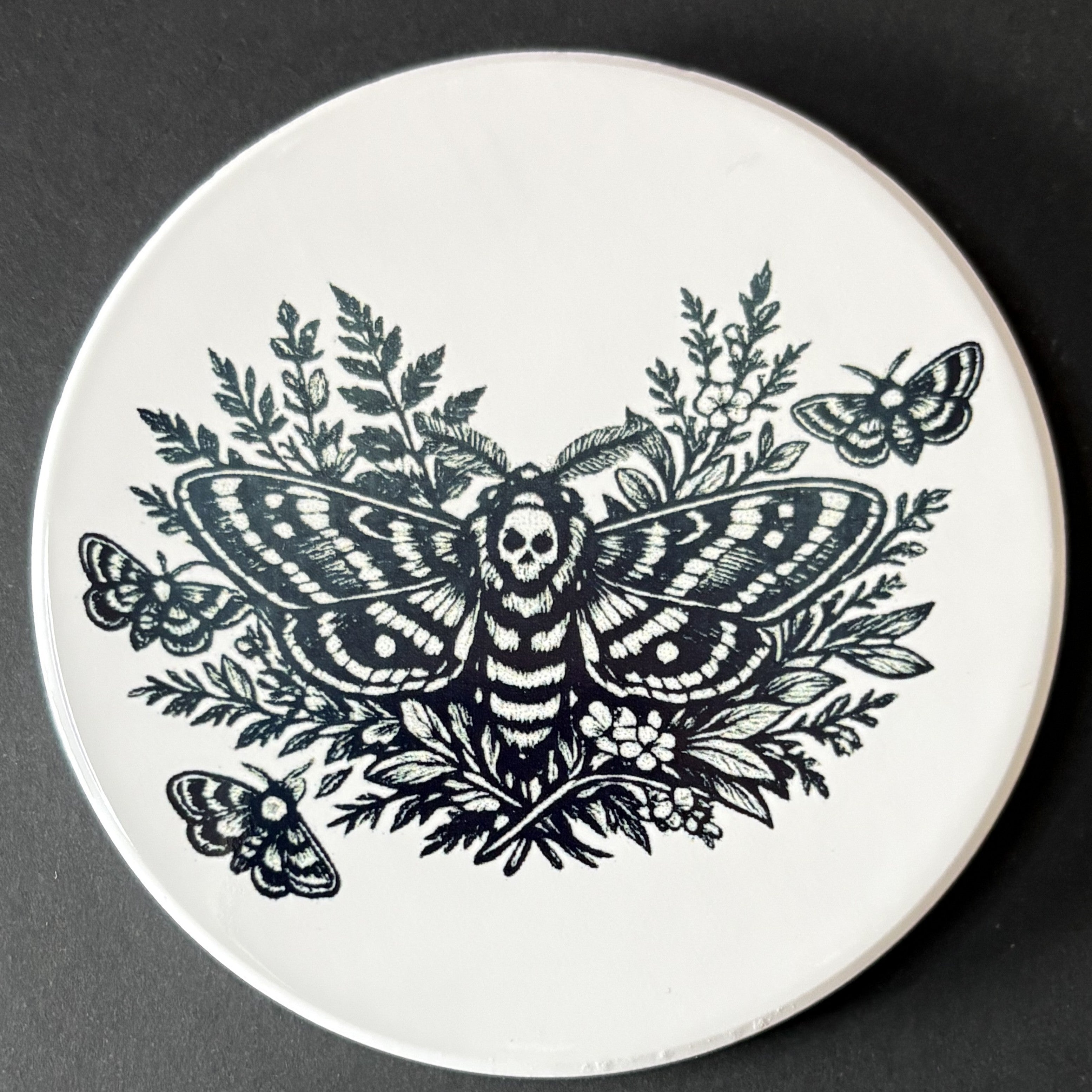Round white plate with black butterfly and floral design on a dark background