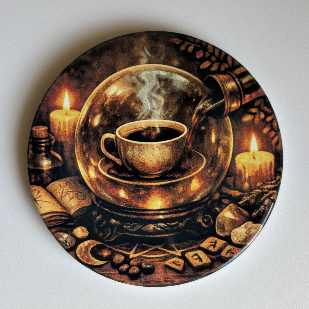 A coaster featuring a mystical illustration of a steaming cup under a glass globe, surrounded by candles, an open book, stones, and magical symbols on a dark background.