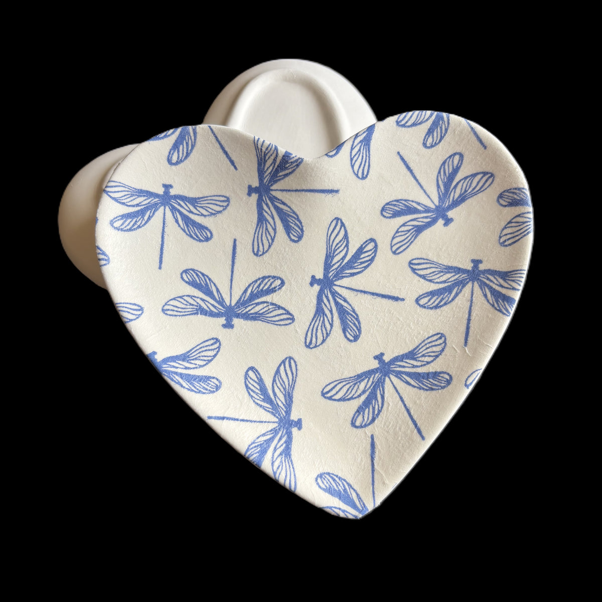 A heart-shaped ceramic Trinket Tray with a blue dragonfly pattern on a white background, shown against a solid black backdrop.