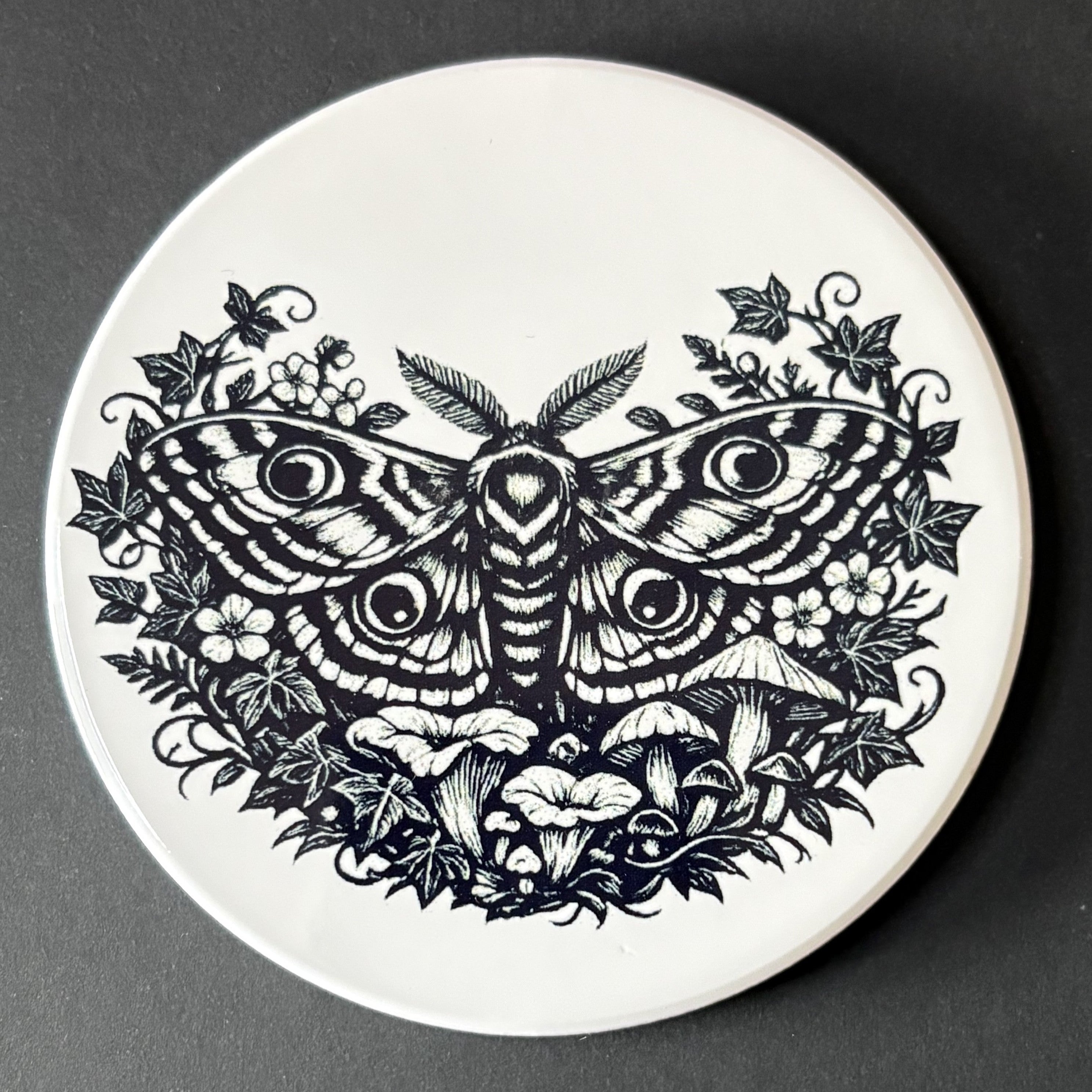 Round coaster with black moth and floral design on a white background