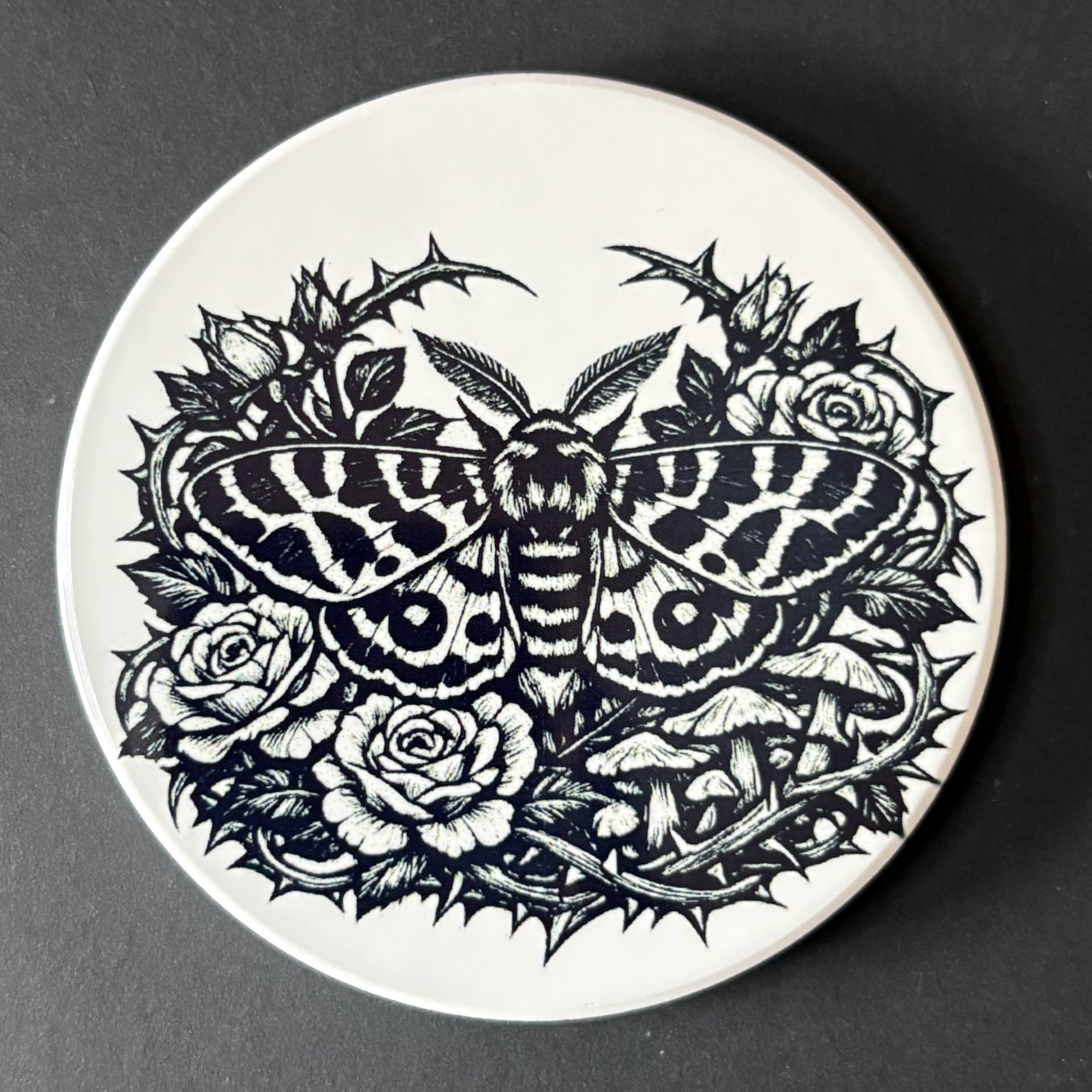 Circular coaster with black butterfly and floral design on a white background