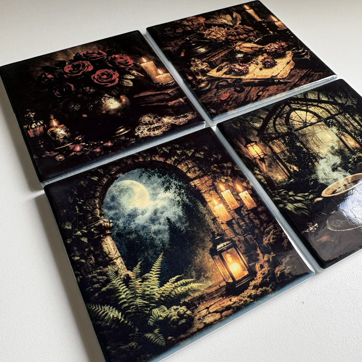 Four square coasters with gothic fantasy illustrations arranged in a 2x2 grid on a white surface. The designs feature dark roses, a candlelit table, a moonlit stone archway with ferns, and a steamy greenhouse scene.