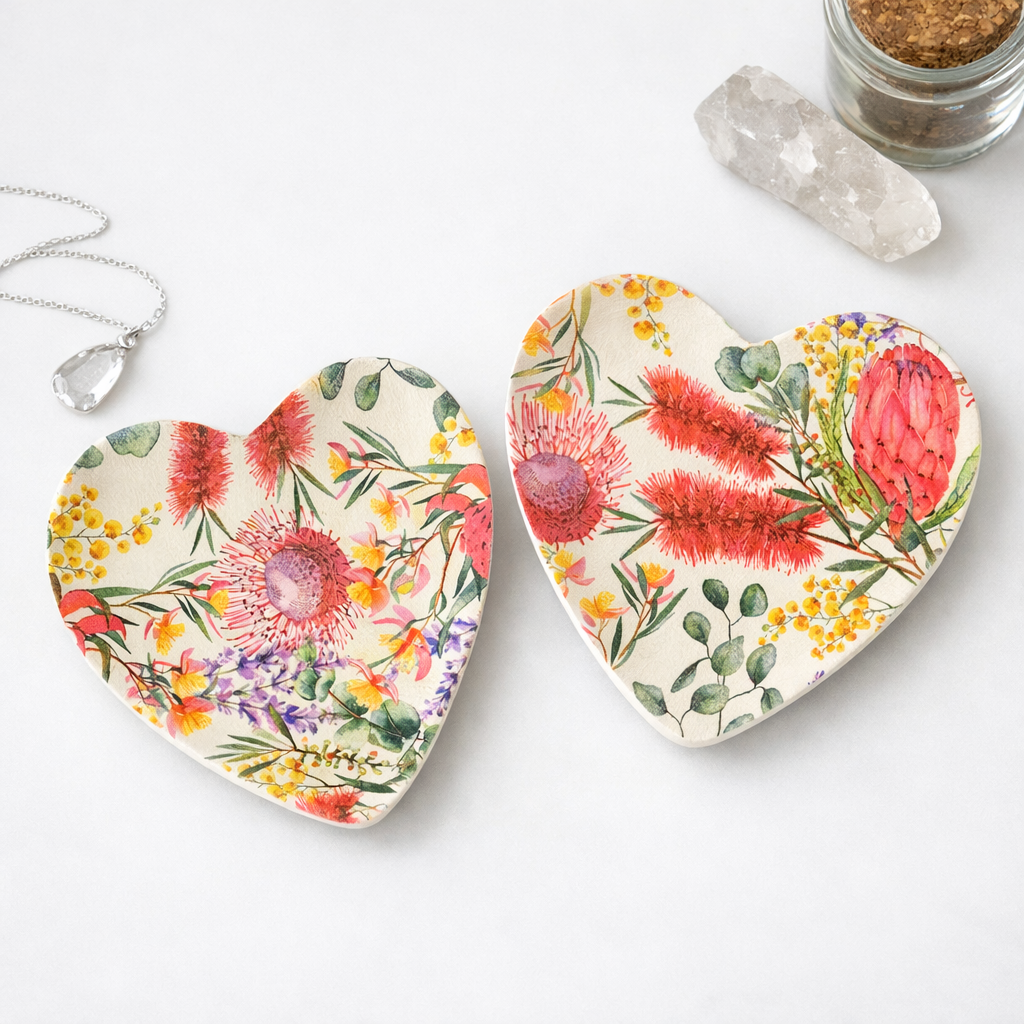 Two heart-shaped ceramic trinket tray with a colorful watercolor floral print, displayed on a white surface with a crystal necklace, a clear crystal, and a small jar of brown beads.