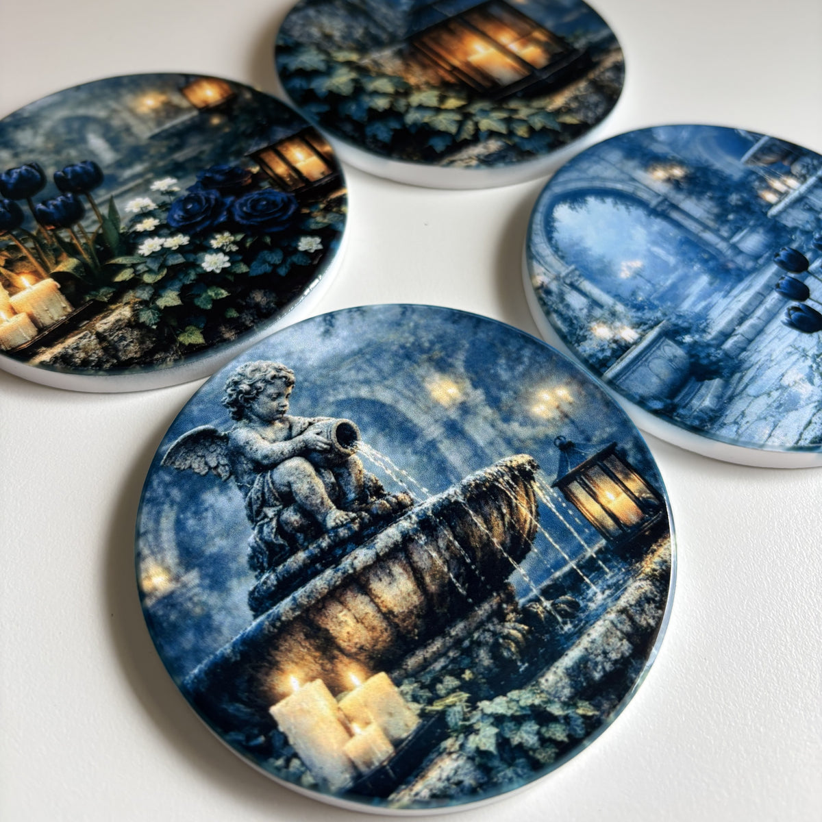 Four round coasters featuring a gothic blue-toned illustration of a fountain with a cherub statue, candles, and flowers, arranged on a white surface.