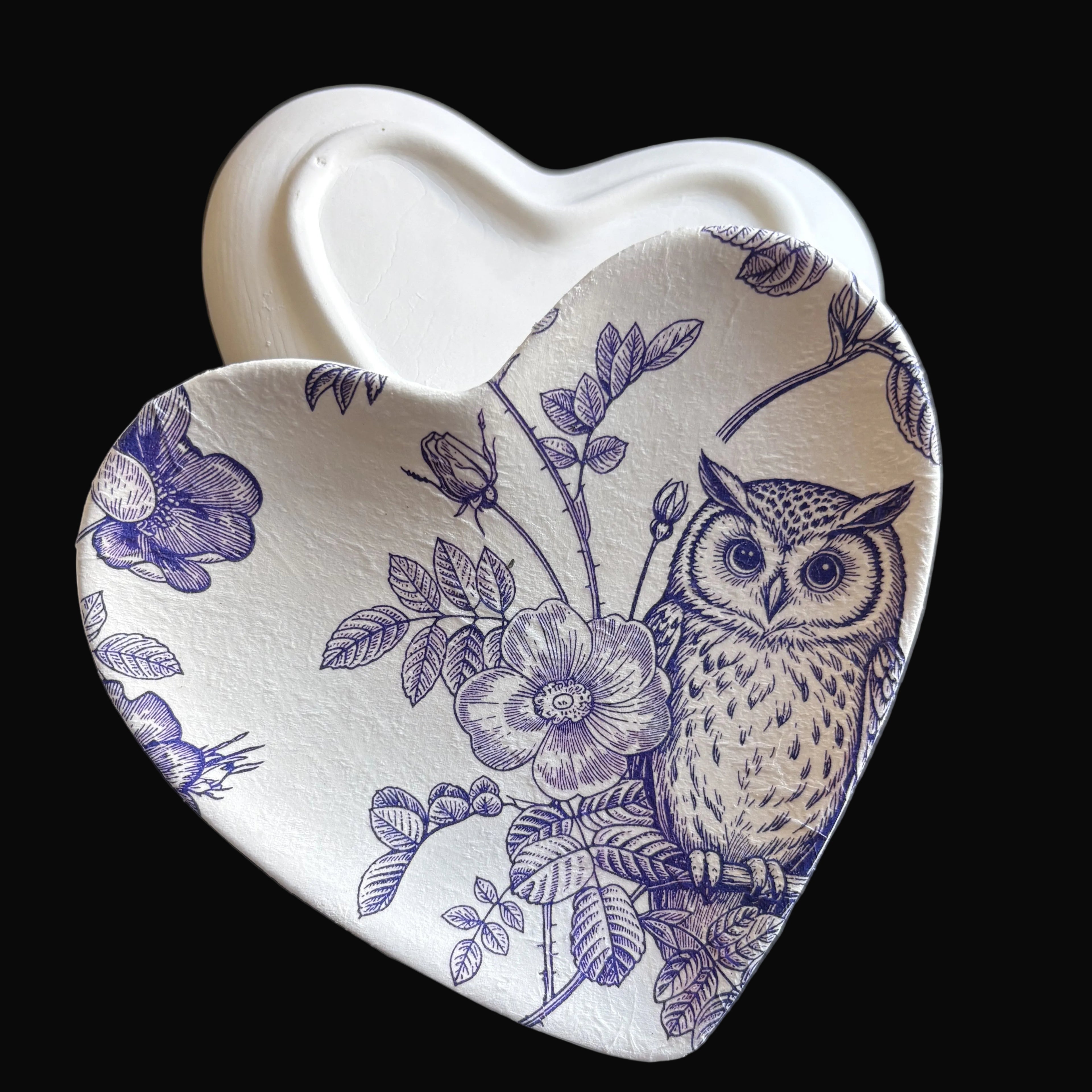 Heart-shaped ceramic dish with a blue floral and owl print on a white background, shown on a dark gray surface with a white heart-shaped object behind it.