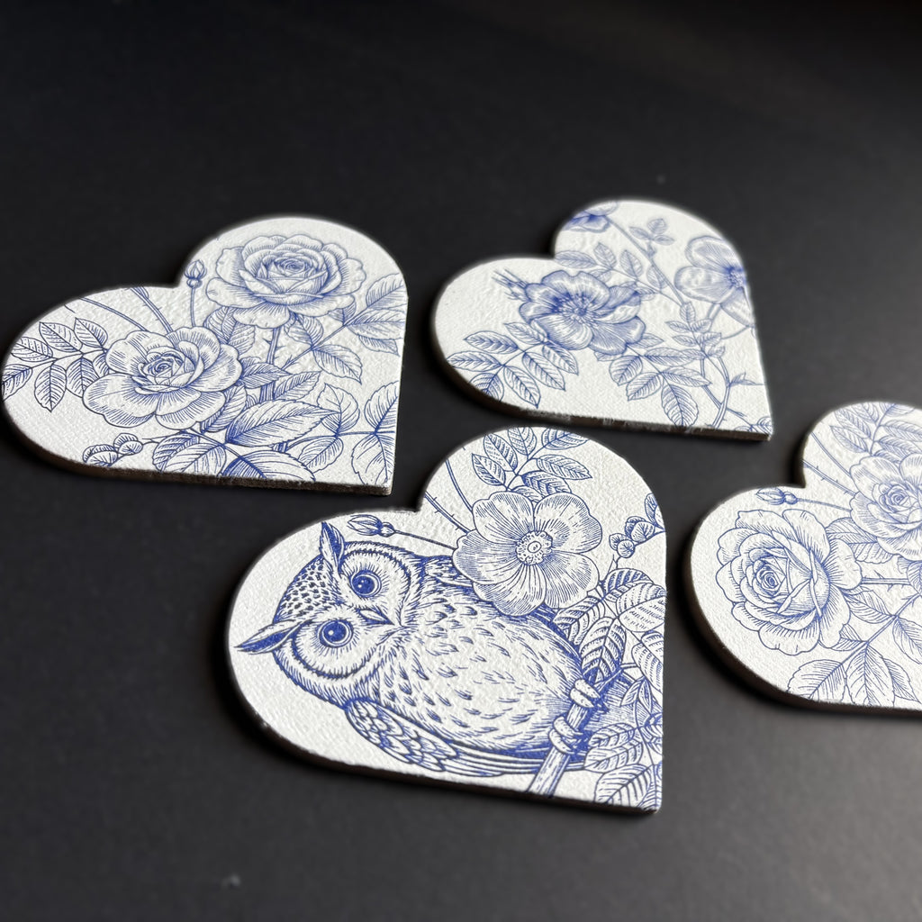 Five heart-shaped magnets with a blue and white floral and owl pattern, arranged on a dark surface.