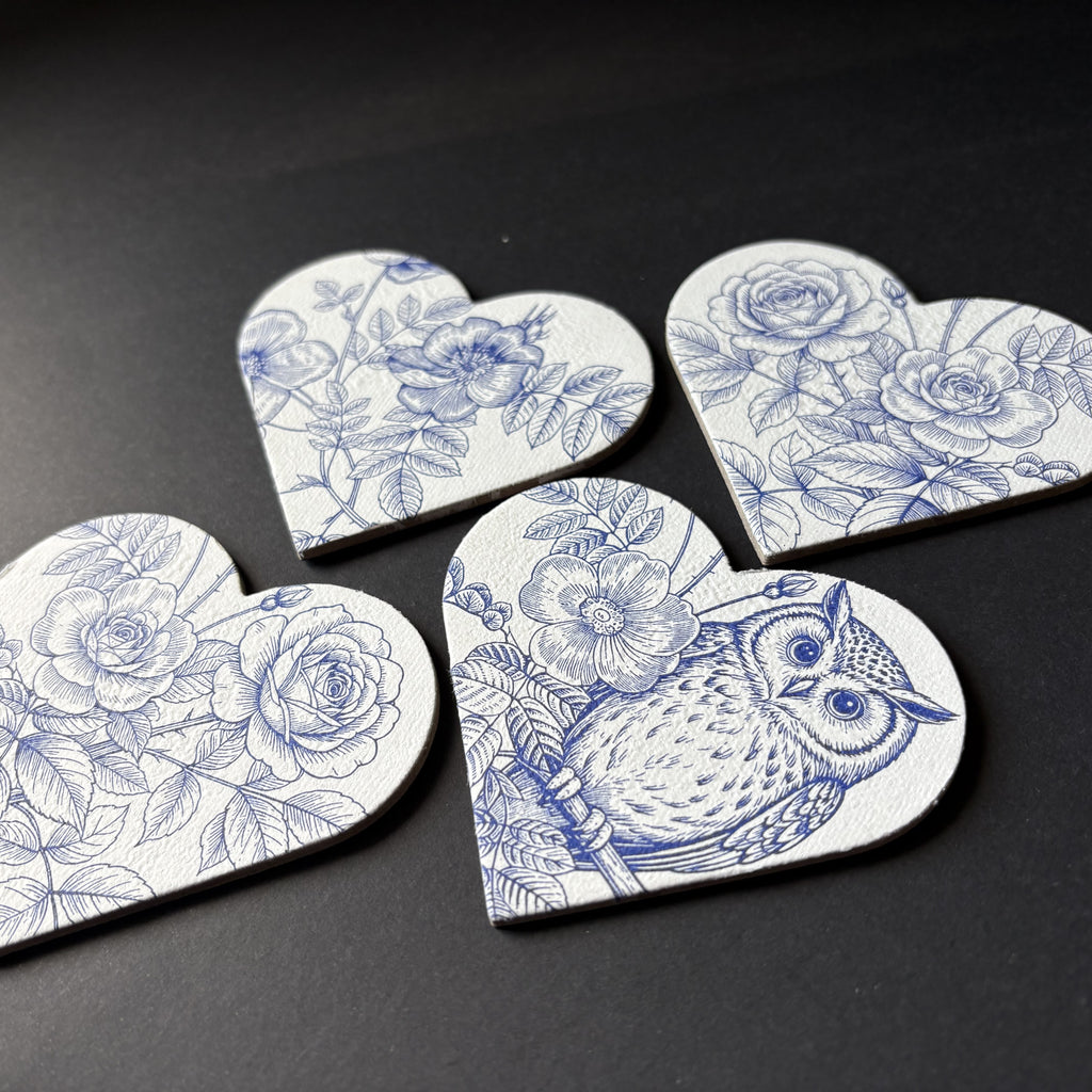 Four heart-shaped magnets with blue floral and owl illustrations on a white background, arranged on a dark surface.