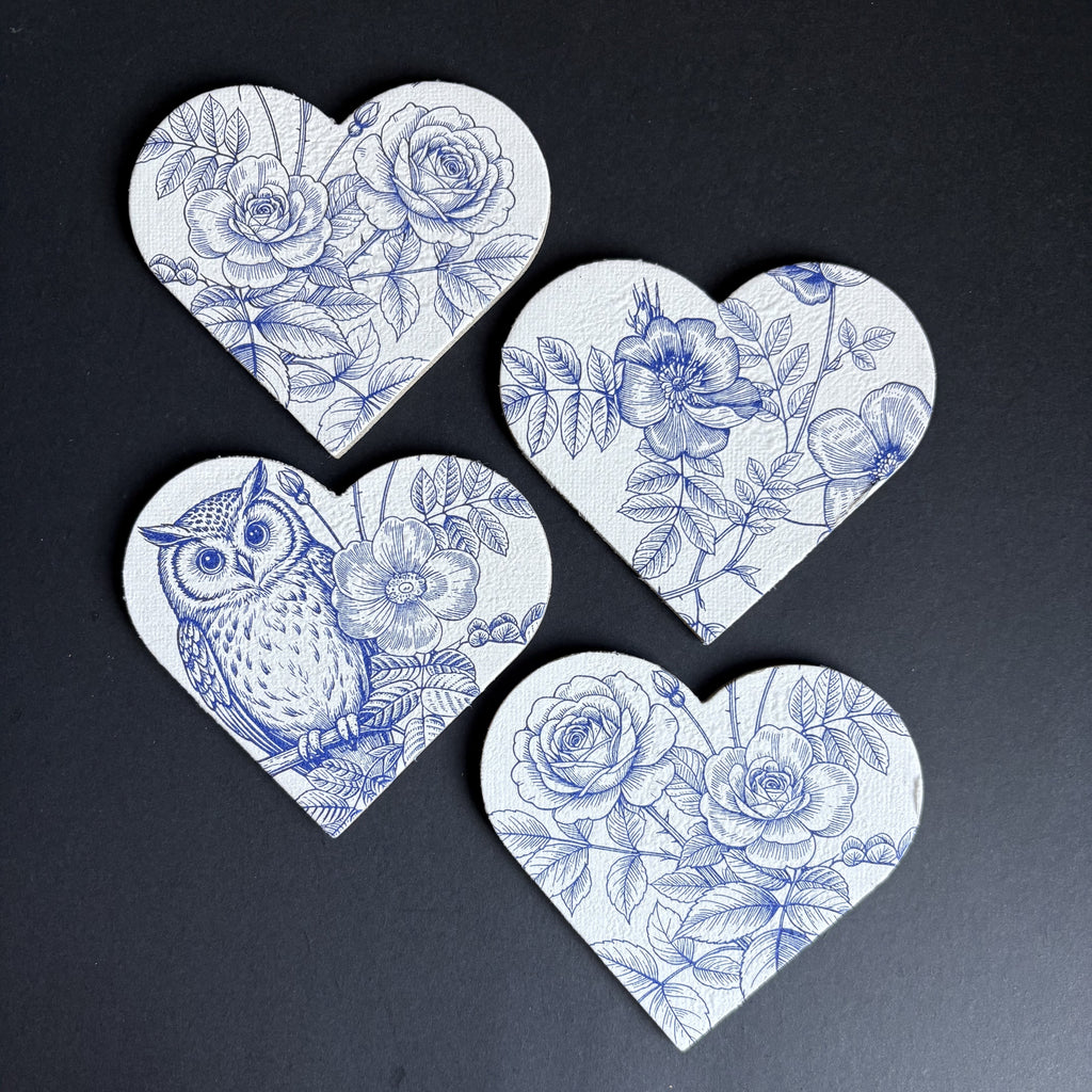 Four heart-shaped magnets with blue floral and owl illustrations on a white background, arranged on a dark surface.