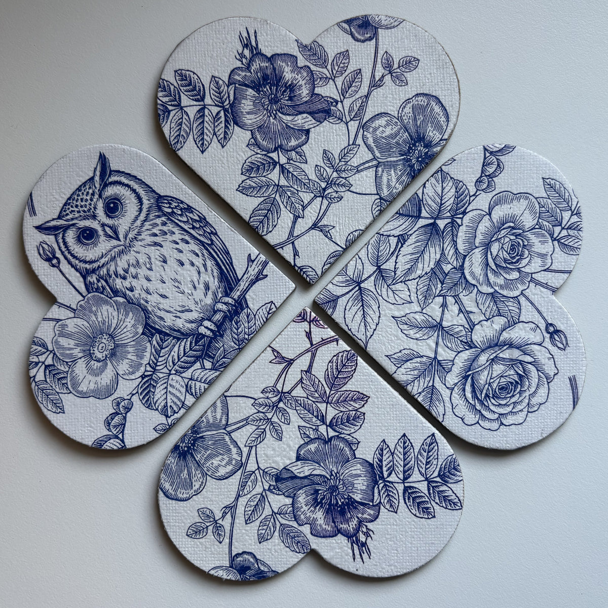 Four heart-shaped magnets with blue floral and owl illustrations on a white background, arranged on a dark surface.
