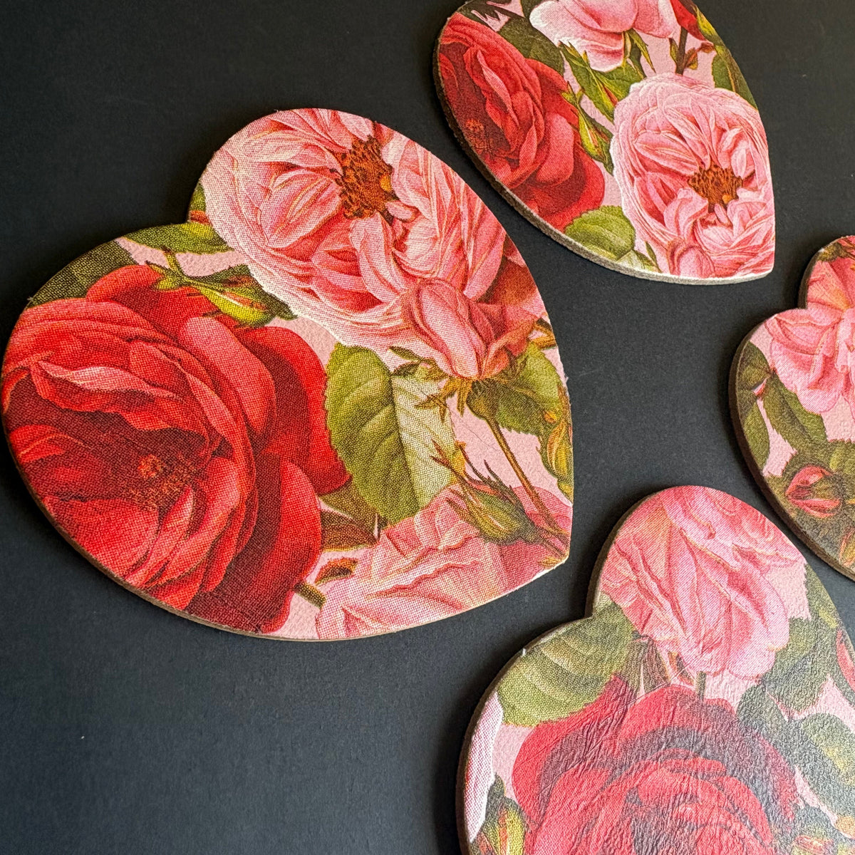 Four heart-shaped magnets with a vintage rose floral print, arranged on a dark gray background.
