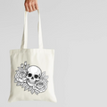 Tote bag with a skull and floral design held by a hand on a light gray background