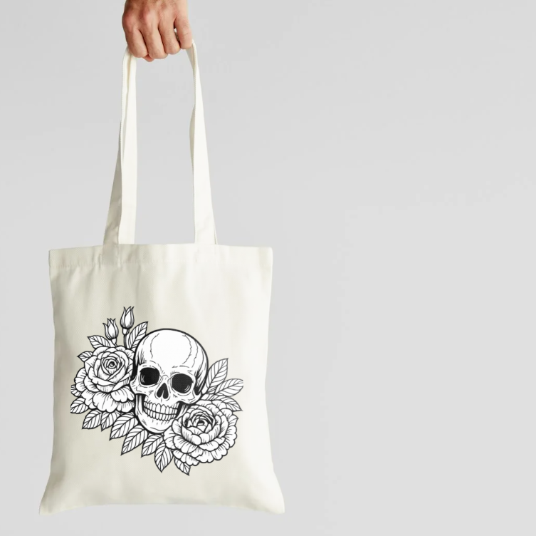 Tote bag with a skull and floral design held by a hand on a light gray background
