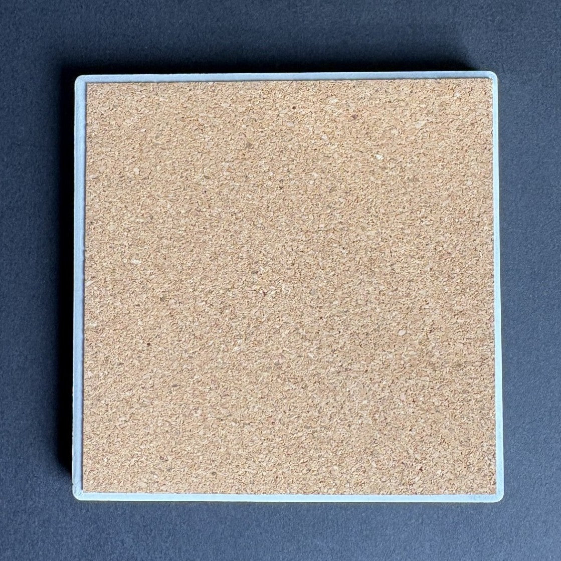 A square cork coaster with a light blue border, shown from a top-down view on a dark gray background.