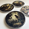 Four round printed coasters featuring dark fantasy and whimsical illustrations, including a cat, a girl in a dress, and a whimsical character, arranged on a light surface.