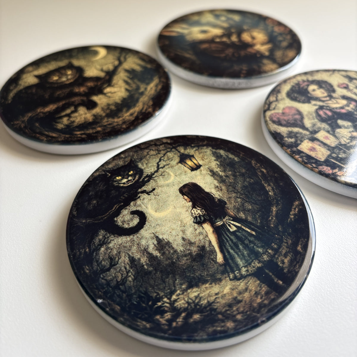 Four round printed coasters featuring dark fantasy and whimsical illustrations, including a cat, a girl in a dress, and a whimsical character, arranged on a light surface.