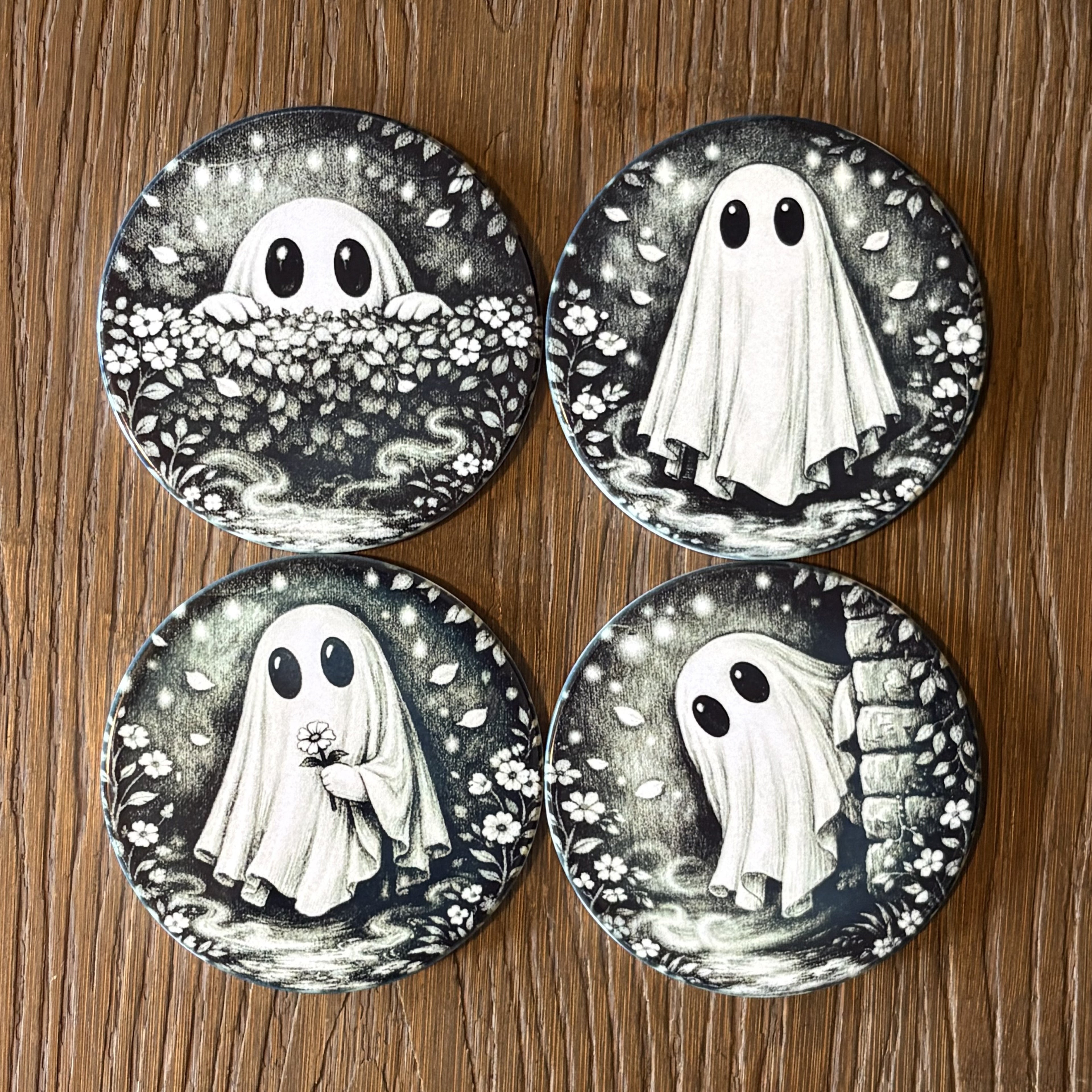 Four round coasters featuring black and white ghost illustrations in different poses, arranged in a 2x2 grid on a wooden surface.