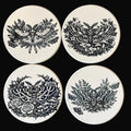 Four ceramic coasters with black moth designs on a dark background