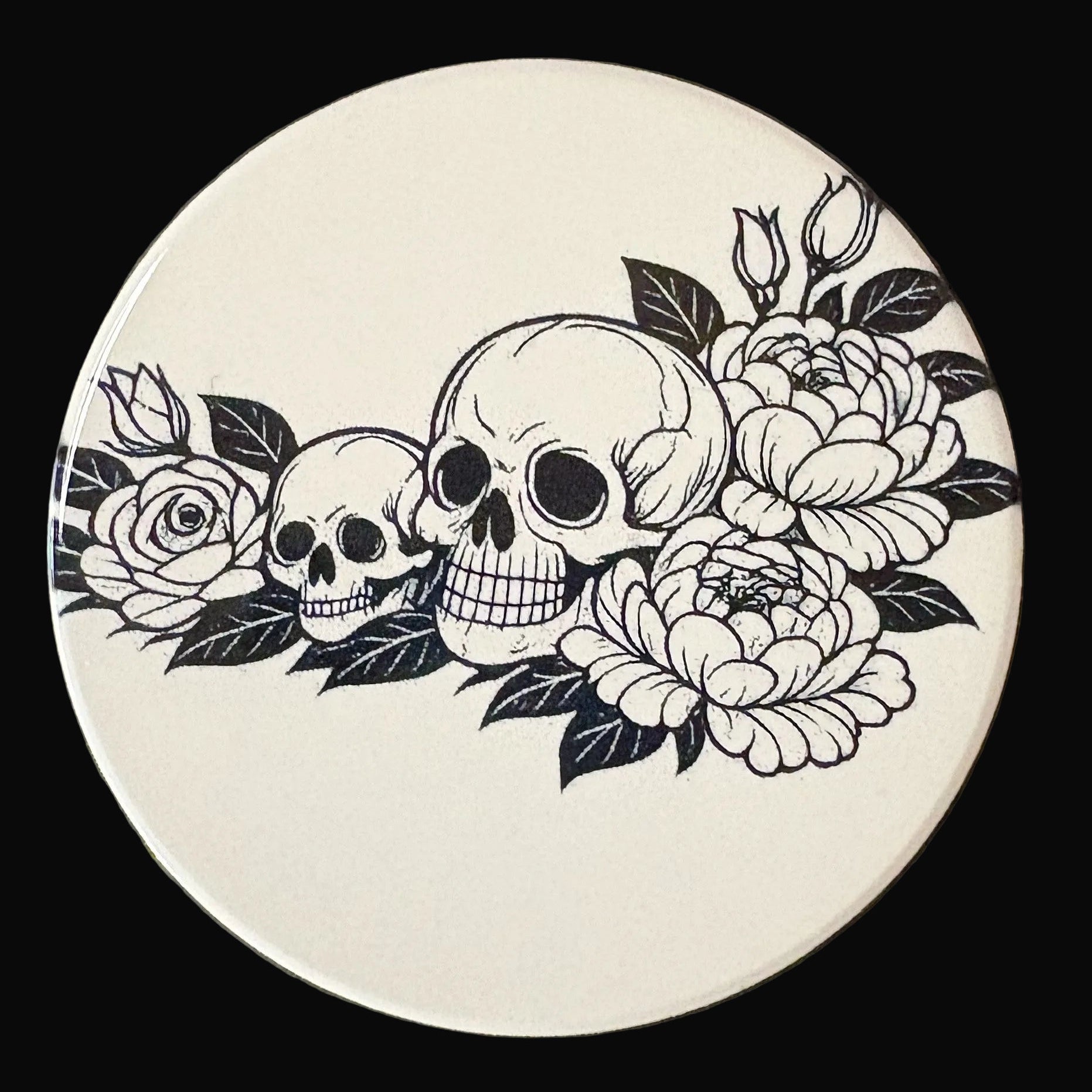 Circular coaster with black and white skull and floral design on a dark background