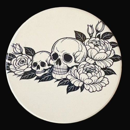 Circular coaster with black and white skull and floral design on a dark background