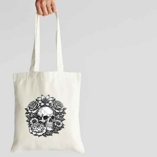 Tote bag with a skull and floral design held by a hand on a light gray background