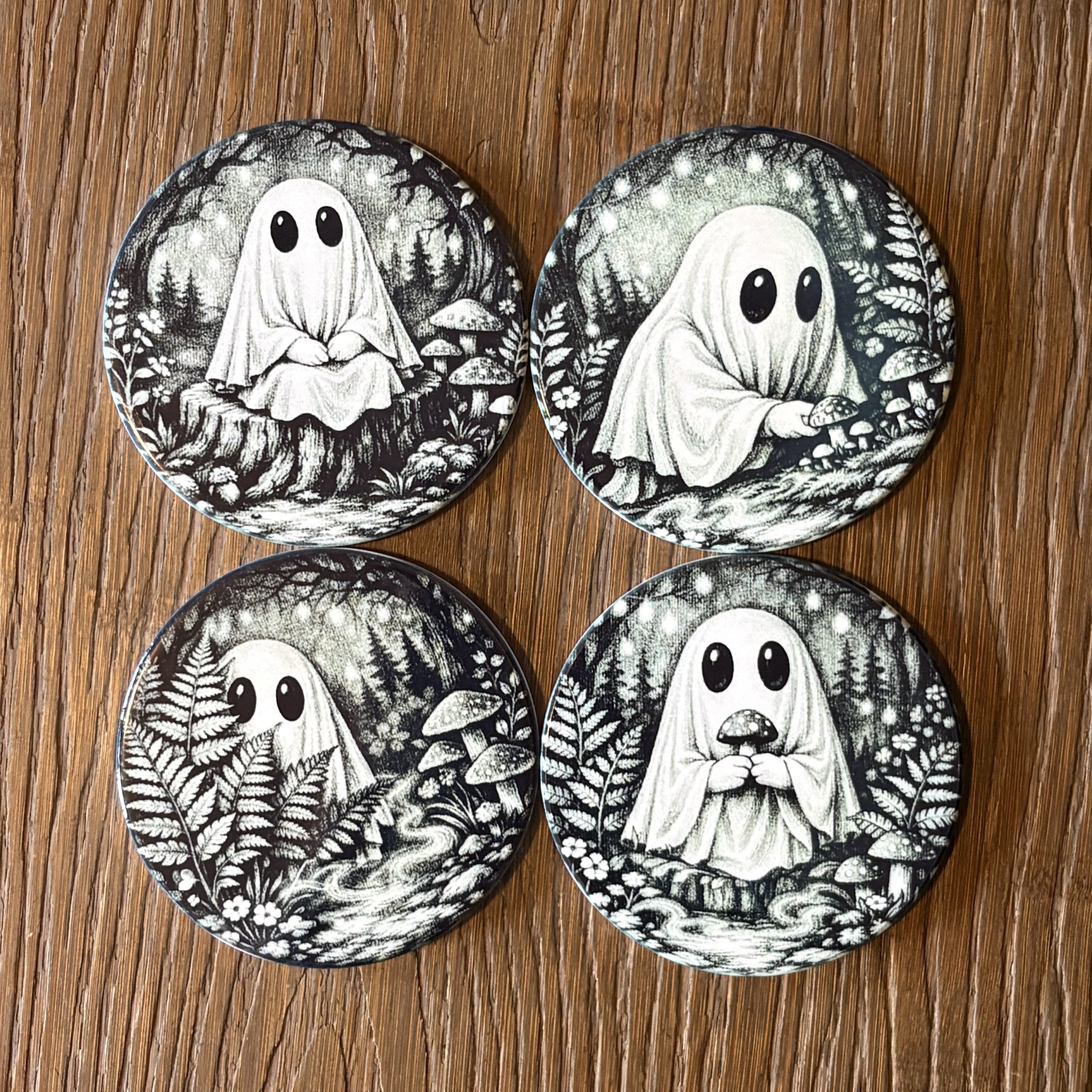 Four round coasters featuring black and white illustrations of cute ghosts in a forest, arranged in a 2x2 grid on a wooden surface.