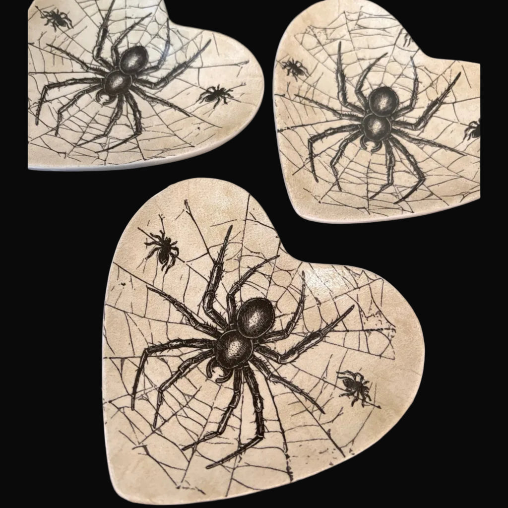 Three heart-shaped ceramic trinket trays with a spider and cobweb design, arranged on a dark background.