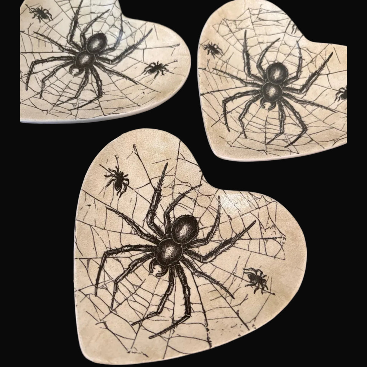 Three heart-shaped ceramic trinket trays with a spider and cobweb design, arranged on a dark background.
