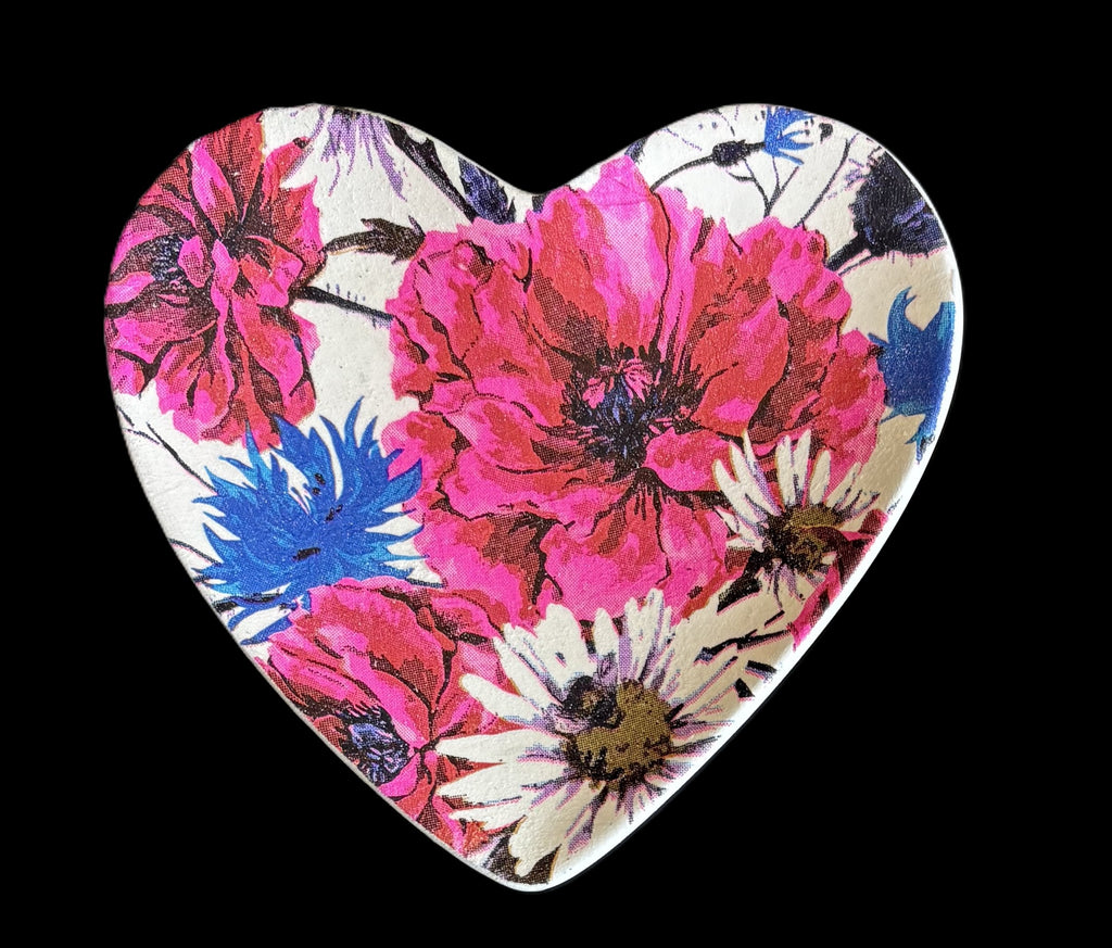A heart-shaped decorative trinket tray featuring a vibrant floral print with large pink and blue flowers on a cream background, set against a solid black backdrop.